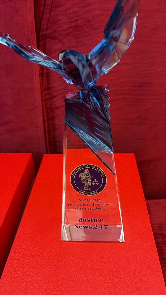 A clear glass trophy featuring a blue eagle figurine on top, engraved with the text 'ACADEMIA DE STIINTE JURIDICE DIN ROMANIA' and 'News247' on a red background.